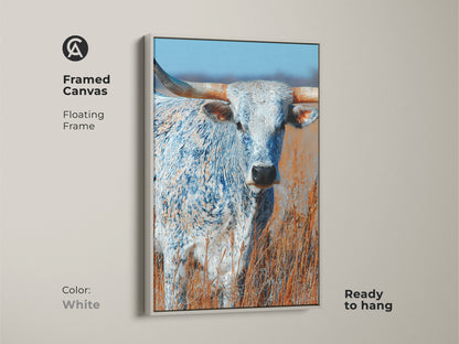 This framed canvas art features a longhorn bull. The artwork has a floating frame. The frame color is white. This canvas print is ready to hang. The animal art is a beautiful addition to any space.