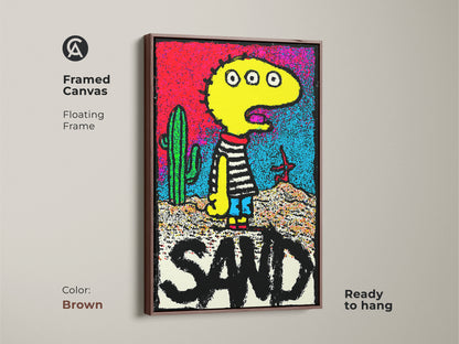 Framed canvas artwork with a floating frame showcasing a quirky yellow character in a desert setting. The art includes a cactus and the word SAND in bold letters. The brown frame complements the artwork. Shop framed canvas art today.