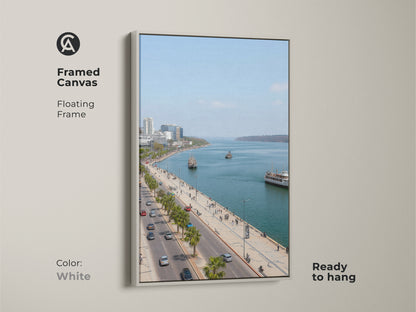 Framed canvas artwork featuring a blue teal coastal cityscape. The white floating frame enhances the travel photography. Palm trees line the street. Perfect for entry hall decor. Contemporary seaside art.