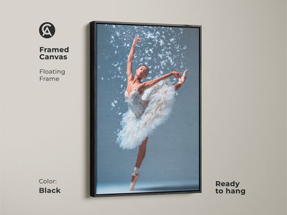 Framed canvas art featuring a ballerina. She is wearing a white tutu. She is en pointe with one leg extended. White feathers accent the artwork. The floating frame is black. This beautiful ballet art is ready to hang.