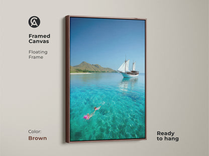 Brown framed canvas art shows a sailboat and snorkeler. The floating frame enhances this coastal art print. Enjoy the turquoise ocean and nautical charm. This artwork creates a relaxing beach vibe.