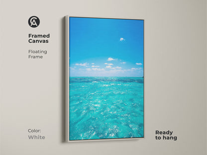 Framed canvas of a turquoise ocean view with a floating frame in white. This coastal beach wall art is ready to hang. The blue sky water artwork is perfect for residential blue art prints. Add a calm ocean wall hanging to your living room.