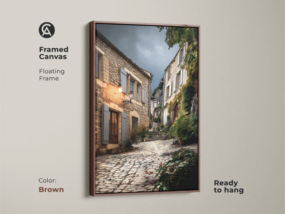 Framed canvas art featuring a rustic European village street. The brown floating frame complements the beige and brown tones. This cobblestone street artwork is ready to hang. Ideal for adding old-world charm to your home. A perfect housewarming gift for travel lovers and countryside painting print.