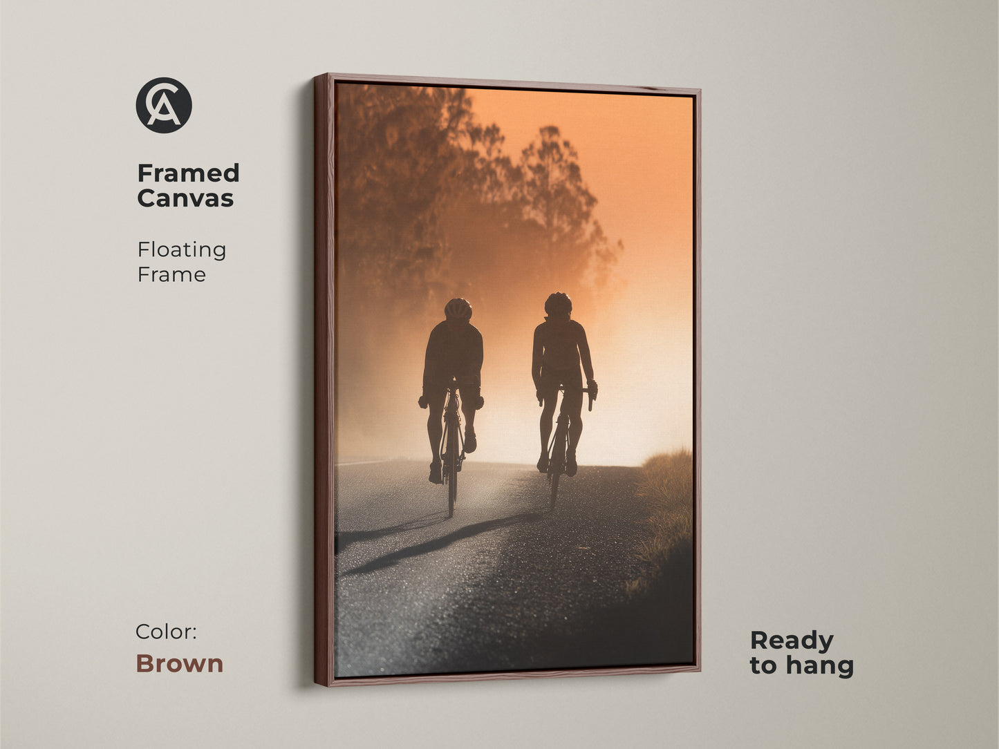 Framed canvas showing a road cyclist silhouette. The artwork features a brown floating frame. This modern sport art displays a warm amber sunset landscape. Ready to hang.