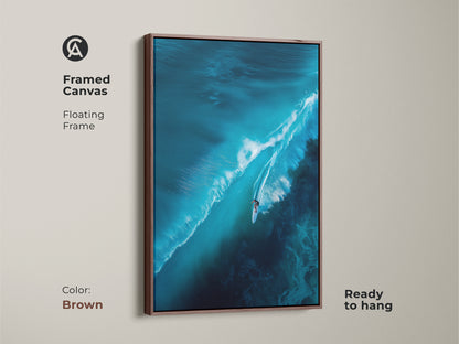 Framed canvas artwork featuring a surfer riding a large wave. The floating frame is brown. This ready-to-hang piece brings warmth to your decor. It's ideal for those who appreciate coastal-themed artwork.