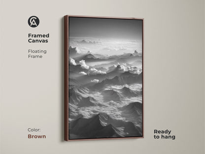 Framed canvas showcasing black and white mountain art. This aerial landscape artwork has a brown floating frame. The minimalist cloudscape wall decor is ready to hang. Great contemporary bedroom print.