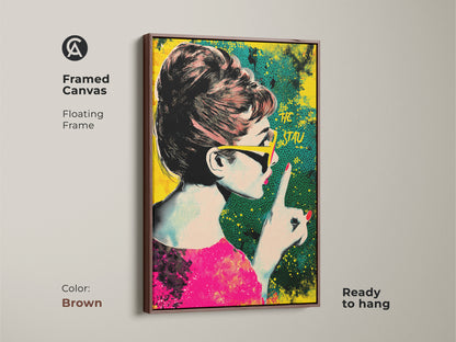 Framed canvas of Audrey Hepburn pop art with a brown floating frame. The artwork showcases a retro halftone style in pink yellow and teal. It is ready to hang. Ideal eclectic home decor.
