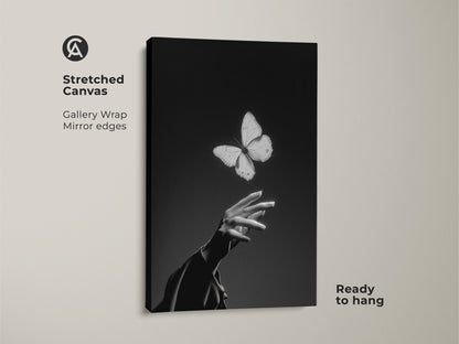 Stretched canvas gallery wrap of a monochrome butterfly art print. It features a minimalist hand. Black and white abstract art shows an insect and human touch. Ready to hang as contemporary bedroom decor. A nature lover gift