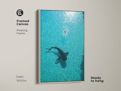 Framed Canvas with a white floating frame displaying an aerial view of a whale shark and swimmer. This minimalist ocean decor brings a touch of coastal charm to your home. Ready to hang. A serene ocean scene in turquoise waters.