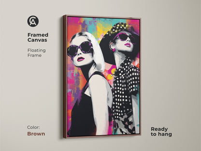 Framed canvas with a brown floating frame displaying pop art artwork of women in sunglasses. The vibrant abstract background combines magenta teal and yellow. This ready-to-hang art piece brings a modern flair to any home. The stylish female portrait is perfect for a chic home office. A colorful abstract wall decor.