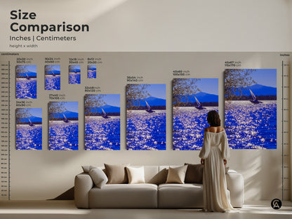 Size comparison of sailboat art prints in inches and centimeters. See how different sizes fit above a sofa. The artwork captures a sailboat on sparkling water with mountains. Transform your living space with this coastal landscape art.