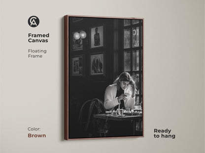 Brown framed canvas of a monochrome cafe scene. This contemporary black and white photojournalism style artwork features a woman with coffee. Ready to hang with a floating frame. Perfect for adding a sophisticated touch to dining rooms and home offices.