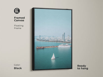 Framed Canvas with a floating black frame showcasing an aerial cityscape. Includes a sailboat cruise ship. Ready to hang. Blue teal artwork adds a contemporary touch.