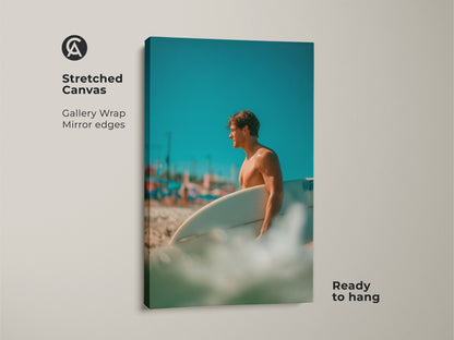 Stretched canvas artwork of a surfer on a beach. Gallery wrap with mirror edges. The image shows a man holding a surfboard with a blue sky. This canvas is ready to hang and enjoy. 