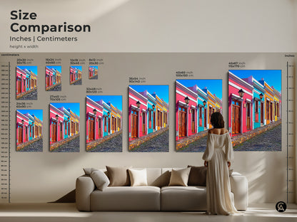 A size comparison shows the colorful houses art print in various sizes for eclectic home decor. This cartoonish travel artwork featuring a European street scene makes a vibrant statement. Sizes range to fit any wall. Perfect as art for a living room or a unique gift for travelers seeking wanderlust wall art.