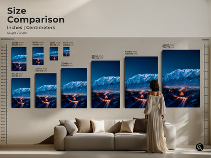 Size comparison of canvas prints. A woman stands near a sofa. The indigo mountains and train art range from 20x30 cm to 45x67 inches. The art becomes a focal point in any room. The blue orange landscape is a modern home gift.