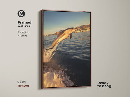Framed canvas art with a brown floating frame of a dolphin jumping. It's ready to hang and complements coastal artwork themes. The artwork features a dolphin leaping from the ocean waves. Bathed in golden yellow sunlight it adds a dynamic focal point to any room.