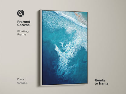 Framed canvas with a white floating frame features deep blue ocean wave art. This turquoise aerial view artwork complements any room. Ready to hang this coastal wall decor is perfect for beach lovers. This modern abstract seafoam art transforms your space. A stunning abstract seascape painting.
