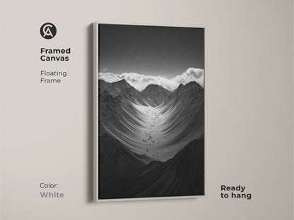 Framed black and white mountain art print with a white floating frame. This monochrome canvas art is ready to hang. The hikers are ascending a vast snowy mountain range. This nature scenery wall art adds adventure to any space.