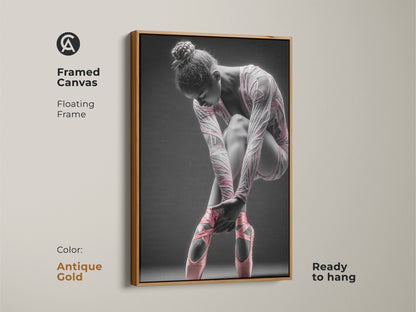 Framed canvas artwork featuring a ballerina. This canvas has a floating frame. The frame color is antique gold. The art features a ballerina tying her pink ballet shoes. This framed art is ready to hang.