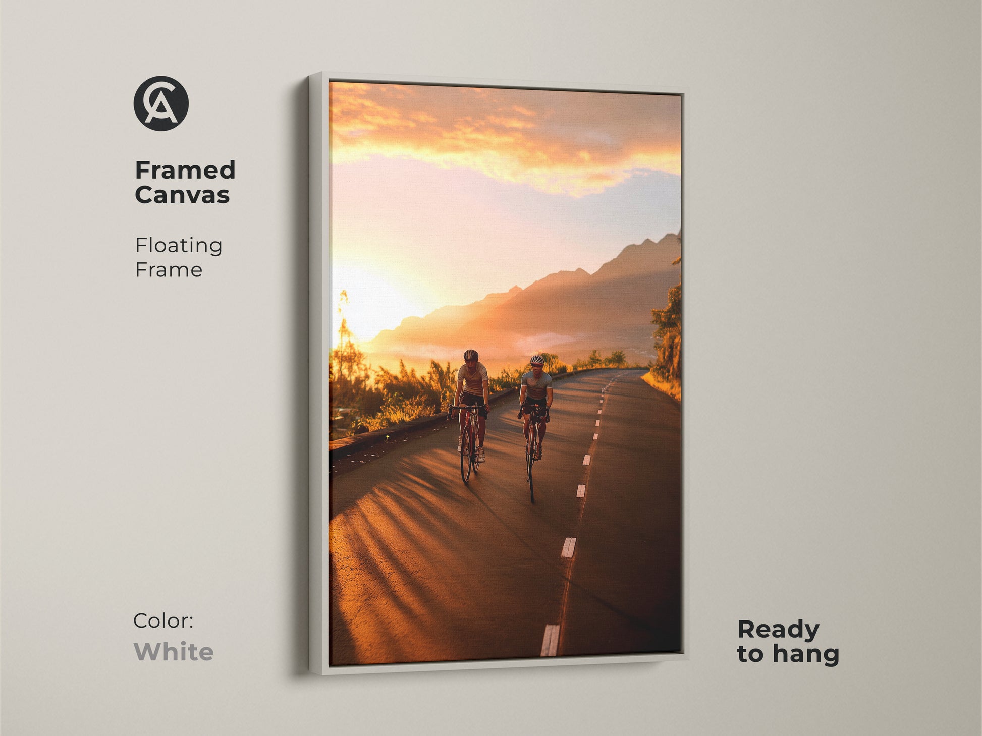 Framed canvas with a white floating frame featuring cyclists on a mountain road at sunset. Ready to hang and complements modern decor. This cycling wall art captures a scenic route in warm yellow and orange hues. Ideal for travel-themed decor and cyclist gifts.
