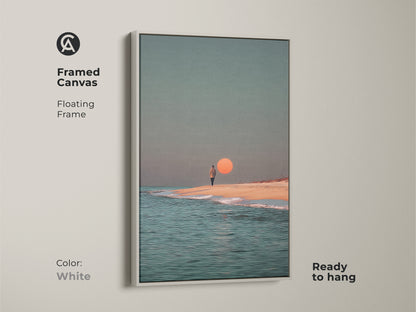 This framed canvas art showcases a minimalist ocean print with a white floating frame. The contemporary coastal wall decor features a person walking on the beach. This surreal sunset beach artwork is ready to hang adding a fresh modern touch.