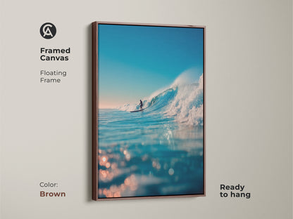 A framed canvas shows a surfer riding a wave. The floating frame is brown and the canvas is ready to hang. This artwork is a beautiful addition to any room. Bring the ocean indoors with this framed artwork.