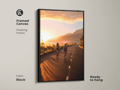 Framed canvas with a black floating frame showcasing cyclists on a mountain road at sunset. Ready to hang and adds a touch of adventure to any room. This cycling wall art brings warm golden orange light to your home. Perfect for contemporary and travel decor.