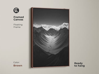 Framed black and white mountain art print with a brown floating frame. This monochrome canvas art is ready to hang. The hikers are ascending a vast snowy mountain range. This nature scenery wall art adds adventure to any space.