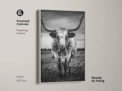 Framed canvas featuring a black and white Texas Longhorn in a floating white frame. This ready-to-hang animal portrait canvas adds character to entryways living rooms or home offices. The rustic ranch decor complements farmhouse or minimalist interiors. It brings a touch of the wild west to any residential space making it an excellent housewarming gift.