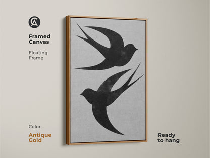 Framed canvas art featuring two black swallows is shown. It is a minimalist wall art with a floating white frame. The monochrome bird artwork arrives ready to hang adding a modern nature touch. Perfect for any room or aesthetic.