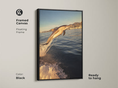 Framed canvas art with a black floating frame showing a dolphin leaping. Ready to hang and perfect for coastal decor. The artwork captures a dolphin jumping out of the ocean. It is a photorealistic style with golden yellow sunlight. This piece adds a dynamic focal point to any room.