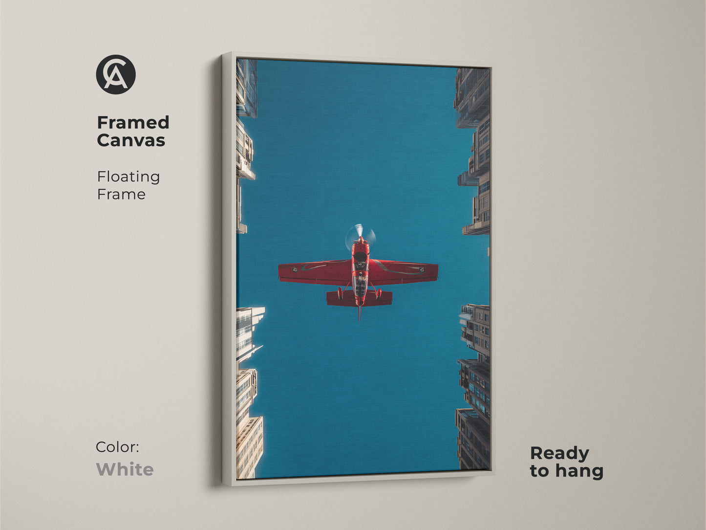 Framed canvas aviation artwork with a white floating frame. A crimson red aeroplane flies through a deep blue sky above urban skyscrapers. Ready to hang. This aviation photography print is a great office decor or a pilot gift idea.
