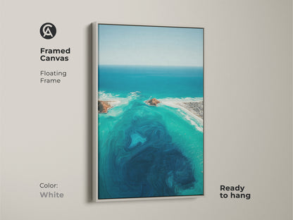White framed canvas of an abstract ocean. This turquoise aerial view artwork is coastal landscape wall art. It showcases deep blue swirls and aqua beach house decor. The floating frame is ready to hang.