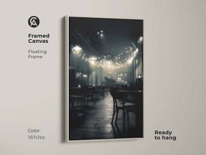 This framed canvas displays a monochrome cafe scene. The clean white floating frame highlights the artwork. String lights illuminate empty tables. Ready to hang this artwork adds sophistication to your home.