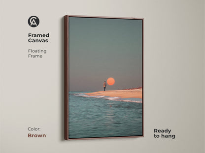 This framed canvas displays minimalist beach wall art with a brown floating frame. The surreal ocean canvas print features a person walking on the beach at sunset. This coastal home decor piece is ready to hang and adds a warm contemporary touch.