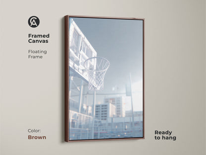 Brown framed canvas art print of a basketball hoop. This floating frame is ready to hang. The low angle shot captures the net. Sunlight shines through the clear backboard. Decorate your home today.