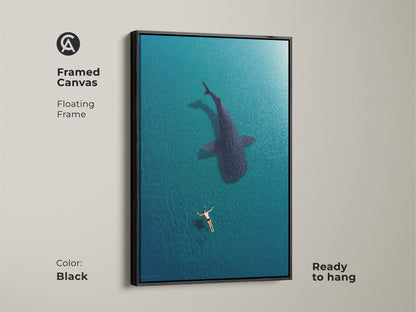 Black framed canvas featuring a swimmer and whale shark aerial art print. This ready-to-hang coastal wall decor adds a modern touch to any room. The deep blue turquoise artwork creates a serene underwater scene for ocean lovers.