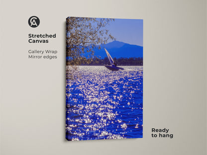 A stretched canvas art print shows a sailboat on blue water. A mountain range is in the background. This gallery-wrapped canvas has mirrored edges. This coastal artwork arrives ready to hang for easy display.