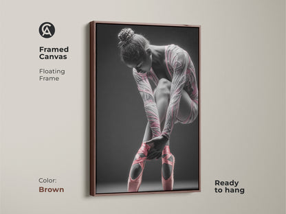 Framed canvas artwork featuring a ballerina. This canvas has a floating frame. The frame color is brown. The art features a ballerina tying her pink ballet shoes. This framed art is ready to hang.