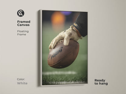 This framed canvas features a close-up of a football player's hand holding the ball. The floating white frame highlights the sports artwork. Ready to hang this canvas is great for a man cave. This art complements any sports enthusiast's space.