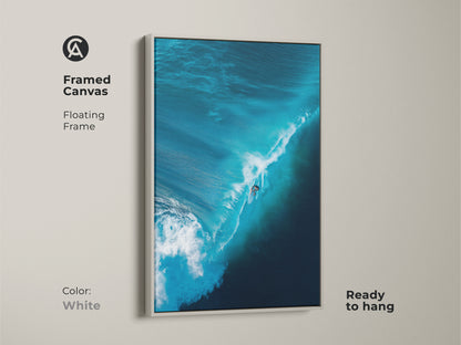 A surfer rides a blue wave in this framed canvas print. The white floating frame complements the artwork. It is ready to hang and brings a fresh look to any room. Ideal for surf art lovers. Order your wave art piece today