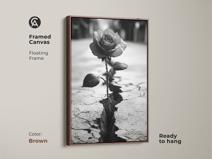 Framed canvas art with a brown floating frame. Showcases a monochrome rose blooming from cracked ground. Symbolizes resilience and nature. The black and white rose art adds a touch of contemporary style. Ready to hang. Perfect as a housewarming gift or symbolic nature decor.
