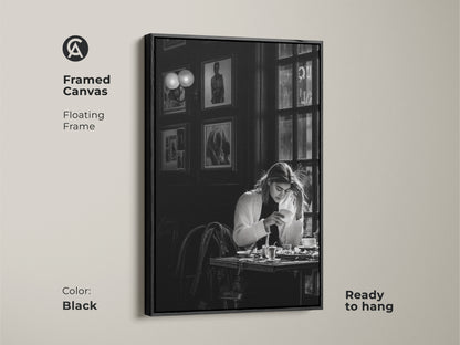 Black framed canvas of a monochrome cafe scene. The contemporary black and white photojournalism style artwork features a woman with coffee. Ready to hang with a floating frame. Enhances modern dining rooms and cafes. Makes a thoughtful housewarming gift.