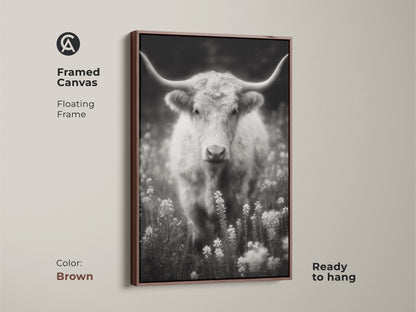 A brown framed canvas print of a longhorn in a field. The black and white artwork is ready to hang. The floating frame complements the rustic style. This fine art photograph is perfect for Western-themed decor.