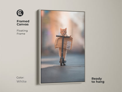 A framed canvas artwork in a white floating frame. The artwork features a ginger cat riding a scooter. This unique piece of cat art is ready to hang in your home.