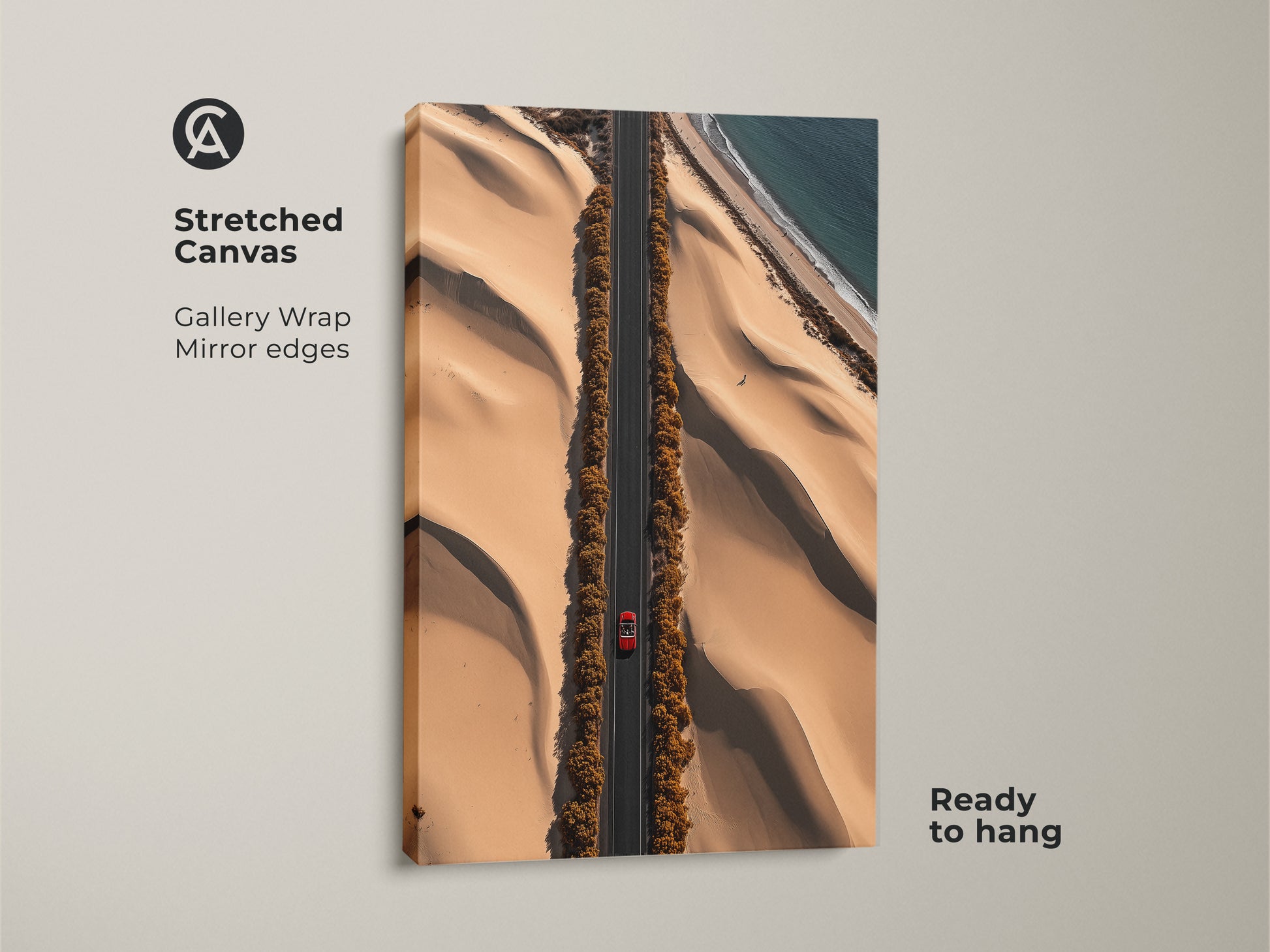 An aerial desert road art print on stretched canvas features a red car. This sandy beige artwork offers a contemporary landscape view of dunes meeting the ocean. Ready to hang this canvas adds a modern travel photography aesthetic to any space. A perfect road trip gift idea for home or office decor.