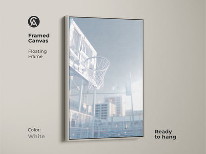 White framed canvas art print of a basketball hoop. This floating frame is ready to hang. The low angle shot captures the net. Sunlight shines through the clear backboard. Decorate your home today.