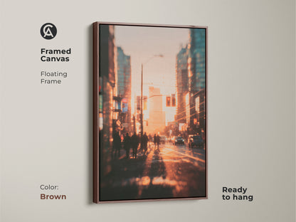 Framed canvas art print of a vibrant city street at sunset. The warm brown floating frame complements the golden hues of the scene. Blurred silhouettes of pedestrians and cars add depth. This ready to hang piece brings modern art to any room. Perfect wall decor.