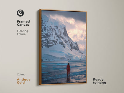 Antarctic canvas print with an antique gold floating frame. This expedition theme home decor shows a lone adventurer in red amid snowy mountains and icy terrain. A striking piece of modern ice blue wall art.